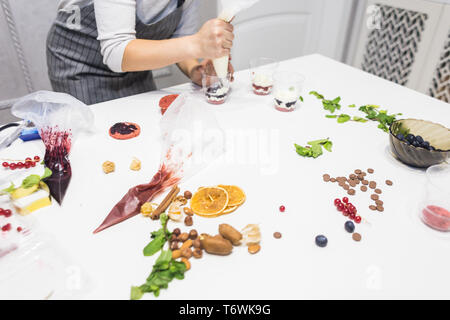 Un pasticcere prepara una inezia in tre tazze. I dessert sono sul tavolo bianco in cucina. Il concetto di dolci fatti in casa, la cottura di torte. Foto Stock