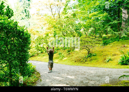 Un giovane ragazzo alza le mani in aria come egli cammina giù per un sentiero Foto Stock