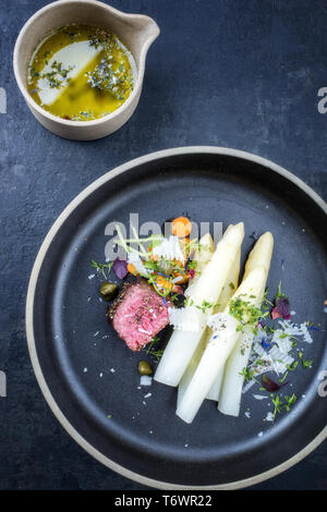 Italiano moderno barbecue invecchiato secco tagliata di manzo con asparagi bianchi e parmigiano come vista dall'alto su una piastra Foto Stock