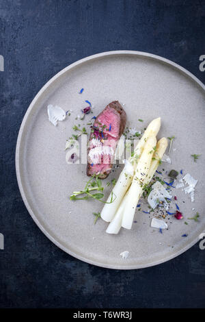 Italiano moderno barbecue invecchiato secco tagliata di manzo con asparagi bianchi e parmigiano come vista dall'alto su una piastra Foto Stock