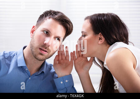 Close-up di giovane imprenditrice Whispering in Partner maschile l orecchio Foto Stock