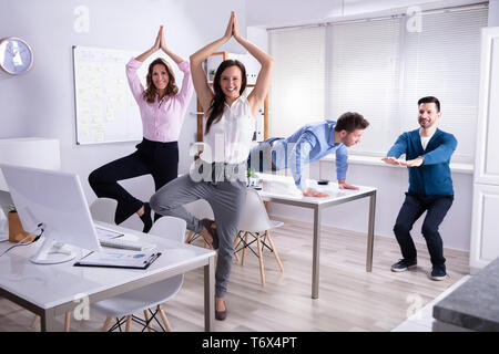 Sorridente Giovani Imprenditori fare yoga in ufficio Foto Stock