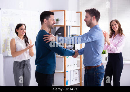 Due partner felice agitando mani mentre altri colleghi battimani in Office Foto Stock