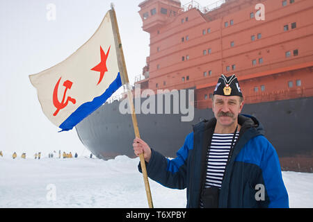 Marinaio russo con bandiera sovietica in piedi accanto alla più grande del mondo di rompighiaccio nucleare 50 anni della vittoria al Polo Nord. Foto Stock