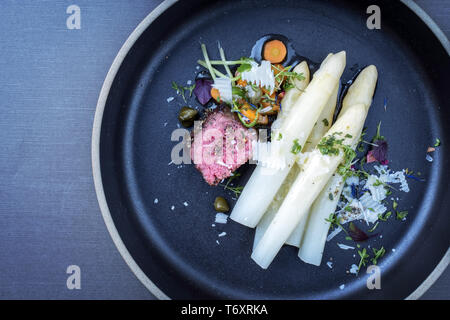 Italiano moderno barbecue invecchiato secco tagliata di manzo con asparagi bianchi e parmigiano come vista dall'alto su una piastra con copia spazio a sinistra Foto Stock
