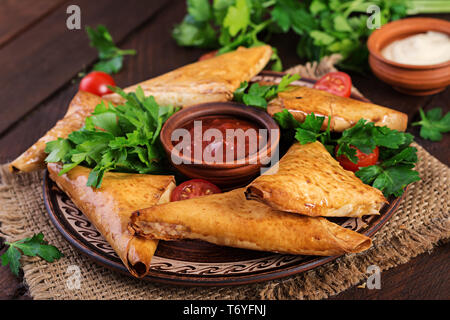 Cibo asiatico. Samsa (samosa) con filetto di pollo e formaggio su sfondo di legno. Foto Stock