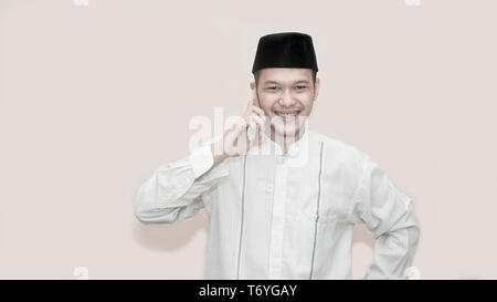 Ritratto di bello musulmani asiatici uomo con cappuccio di testa e utilizza lo smartphone tenendo una chiamata e sorridere alla telecamera - immagine Foto Stock