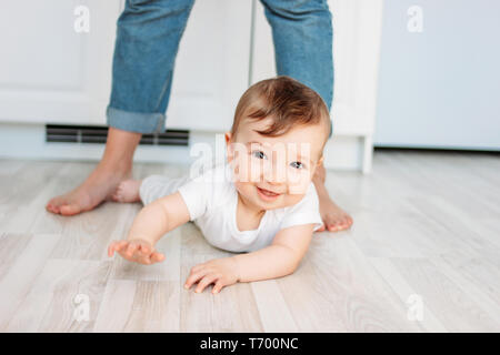 Affascinante piccolo ragazzo 6 mesi sorridente e guardando la telecamera sullo sfondo della mamma del piede Foto Stock