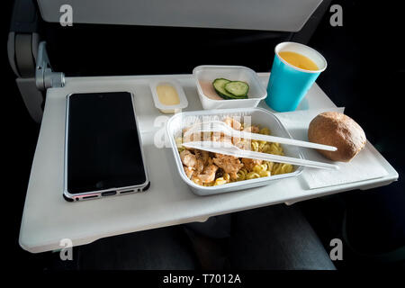 Varie classe economica e alimentare un passeggero smartphone con una schermata vuota sul tavolo pieghevole del velivolo. Pasti a bordo dell'aeromobile. C in plastica Foto Stock