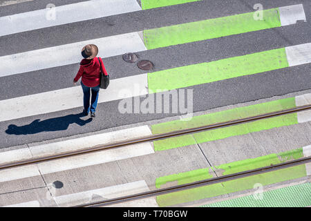 Eleganti Donna slanciata in un cappello rosso, cardigan e jeans attraversa la strada su una zebra attraversamento pedonale rispettando le regole della strada per proteggere il vostro Foto Stock