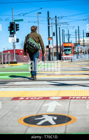 Giovane uomo con sacco sulle spalle attraversa i binari del tram all'intersezione dell'attraversamento pedonale con grafica a colori marcatura per pedoni Foto Stock