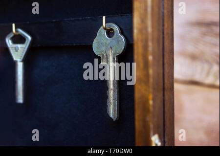 Chiavi appeso sul Golden ganci in una parete titolare di chiave sul legno rustico sfondo. Ipoteca, assicurazione, il concetto di sicurezza. Foto Stock