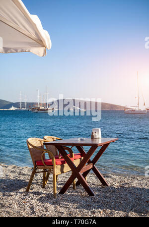 Carino tavolo e sedie e ombrellone in spiaggia al ristorante sul mare a bodrum, Turchia Foto Stock