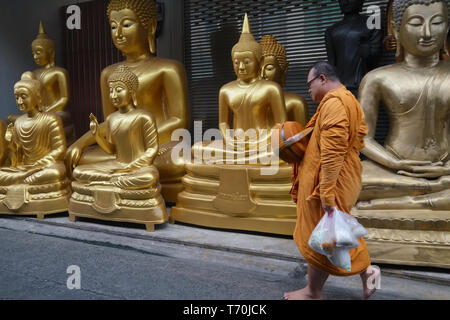 Un monaco buddista passa statue di Buddha al di fuori di una fabbrica per la produzione di oggetti religiosi in Bamrung Muang Road, Bangkok, Thailandia, pronto per la consegna Foto Stock