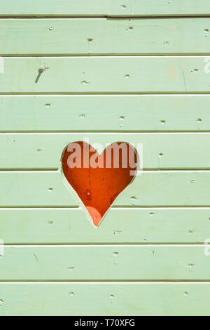 Cuore rosa tagliato a lato di una luce di legno verde beach hut Foto Stock