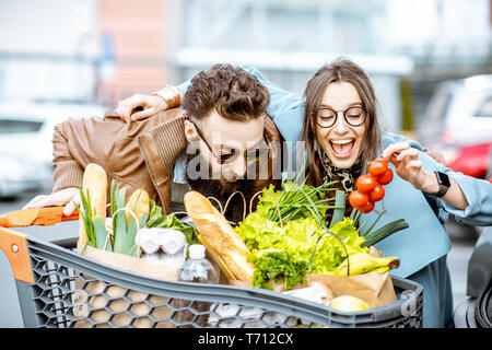 I giovani e la coppia felice con il carrello pieno di prodotti freschi e salutari all'aperto Foto Stock