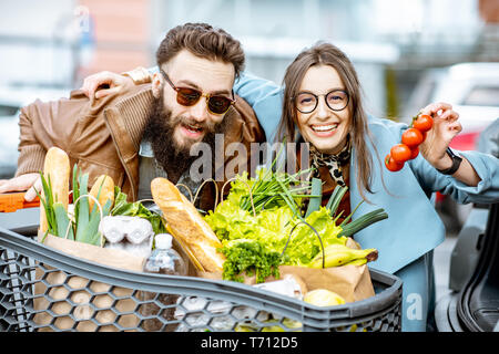 I giovani e la coppia felice con il carrello pieno di prodotti freschi e salutari all'aperto Foto Stock