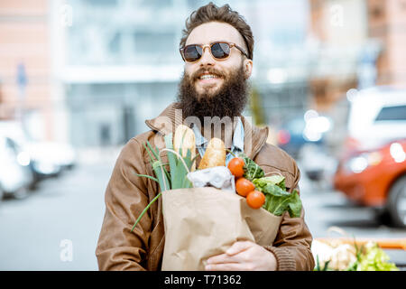 Felice l'uomo elegante con le borse della spesa piena di prodotti freschi e salutari all'aperto vicino al supermercato Foto Stock