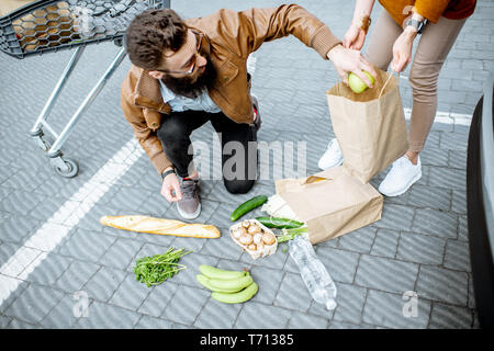 L'uomo aiutando a prendere i prodotti caduto dal suolo sul parcheggio nea il supermercato Foto Stock