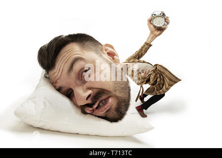 Nessun tempo per la colazione di nuovo. Grande testa sul piccolo corpo giacente sul cuscino. Uomo in tuta home azienda allarme non può svegliarsi "provocare mal di testa e overslept. Concetto di business, di lavoro, dei limiti di tempo. Foto Stock