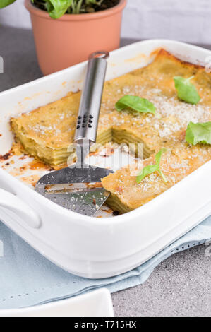 La cucina tradizionale italiana per il pranzo. Lasagne al pesto e basilico. Piatti bianchi sul tavolo. Foto Stock