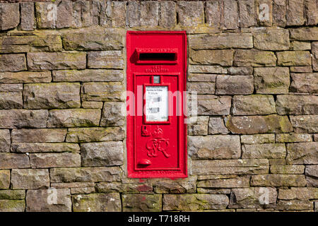 Red Royal Mail postbox su un territorio rurale in pietra a secco parete. In formato verticale Foto Stock