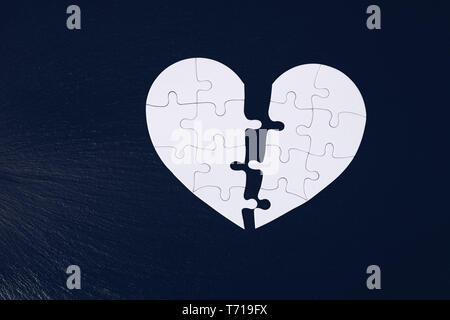 Puzzle di cuore diviso a metà, il giorno di san valentino, due piece jigsaw amore cuore puzzle, amore concetto. Puzzle cuore nero su sfondo di legno. A forma di cuore j Foto Stock