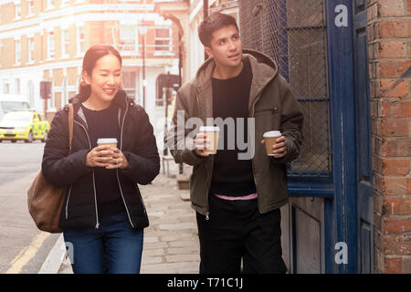 Felice madre con figlio di camminare sulla strada con il caffè da asporto in ci le mani. Foto Stock