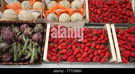 Stallo del fruttivendolo con scatole piene di frutta e verdure come le fragole i meloni e i carciofi appena raccolti dal campo coltivato Foto Stock