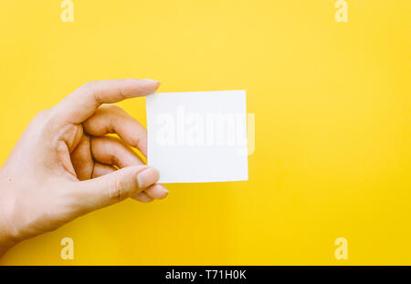 Mano che tiene la carta su sfondo giallo Foto Stock