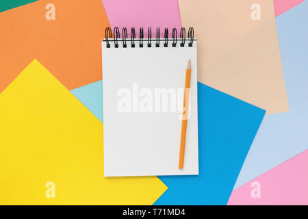 Aprire il notebook con orange matita su un multi colore sfondo della carta. Vista da sopra con copia spazio. Foto Stock