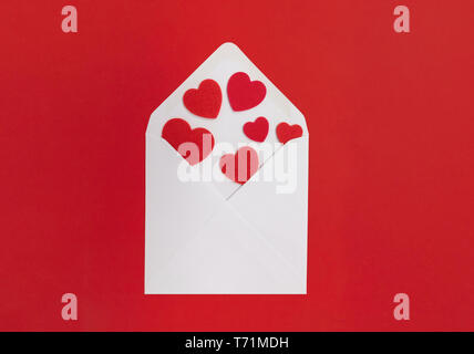 Lettera d'amore concetto. Busta bianca con cuori fuoriuscita, con uno sfondo rosso. Foto Stock