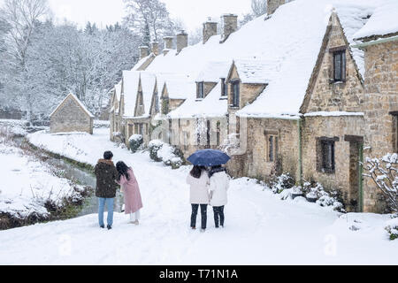 Toursits scattare foto e a piedi arounbd il villaggio di Bibury e la fila di case noto come Arlington Row, raffigurata qui in gennaio nevicata. Foto Stock