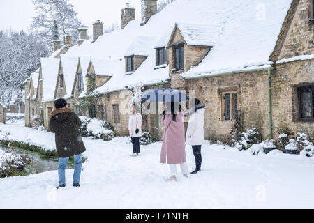 Toursits scattare foto e a piedi arounbd il villaggio di Bibury e la fila di case noto come Arlington Row, raffigurata qui in gennaio nevicata. Foto Stock