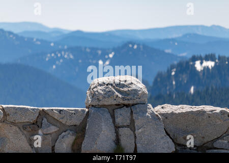 Un basso muro di pietra separa la strada da un enorme cali di corrente con le montagne sullo sfondo in Mt Rainier National Park, nello stato di Washington. Foto Stock