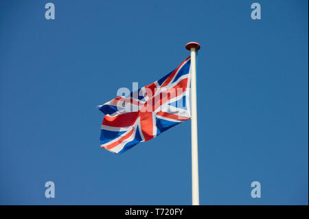 Union Jack, bandiera del Regno Unito sbattimenti nel vento. Blue sky in background. Foto Stock