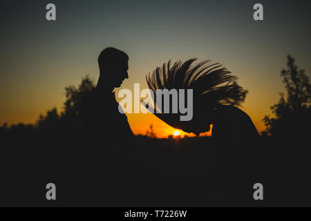 Sagome di coppia felice jumping con bracci sollevati nei pressi del lago al tramonto. giovane vicino al tramonto, persone, craazy Foto Stock