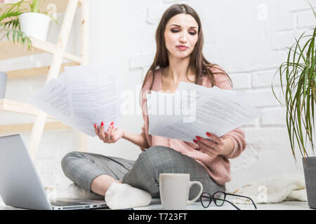 Donna felice esamina la carta seduti vicino al computer portatile, la ragazza freelancer funziona con i documenti. Studente ragazza prende l'istruzione in remoto tramite internet Foto Stock