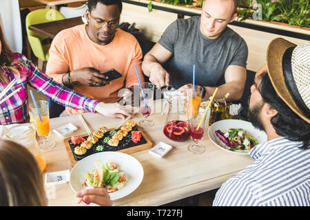 Una società di società multiculturale dei giovani in un cafe mangiare sushi rotoli, bere bevande aventi fun Foto Stock