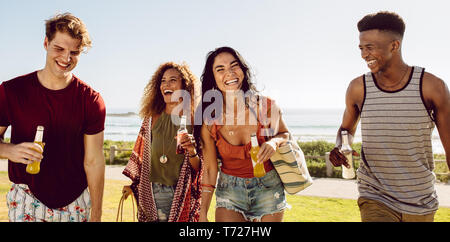 Allegro gruppo di uomini e donne a passeggiate all'aperto con birre. Amici avente un grande momento insieme all'esterno. Foto Stock