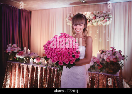 Sposa felice con un grande mazzo di rose. bellissima giovane sposa sorridente trattiene grandi bouquet di nozze con il Rosa Rose. Nozze in rosy e toni di verde. Foto Stock