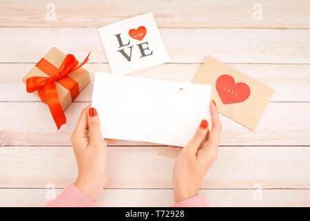 Il giorno di San Valentino amore lettera su sfondo di legno. Velluto rosso a forma di cuore biscotti, caramelle e caffè. Mani femminili con rosso smalto per unghie Foto Stock