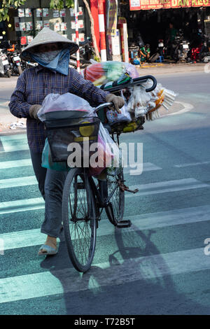 La città di Ho Chi Minh, Vietnam - Marzo 30th, 2019 - Femmina vietnamita cibo di strada venditore attraversando la strada in città con la sua bicicletta. Foto Stock