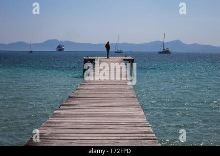 Un uomo si erge su un pontile in legno in Port d'Alcudia, Mallorca, Spagna. Foto Stock