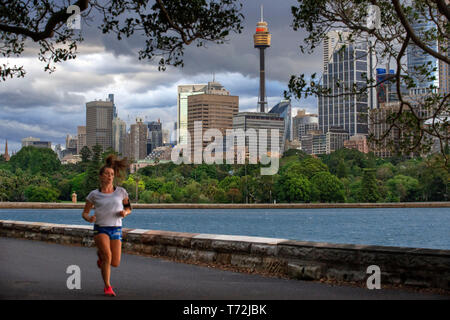 La Torre di Sydney Eye e la donna in esecuzione in Circular Quay promenade e i giardini botanici di Sydney, Nuovo Galles del Sud, Australia Foto Stock