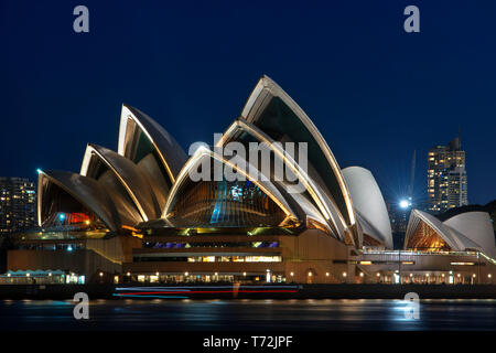 Opera House e il CBD della città al tramonto. Illuminata arco del ponte riflettendo in acque sfocata Sydney, Nuovo Galles del Sud, Australia Foto Stock
