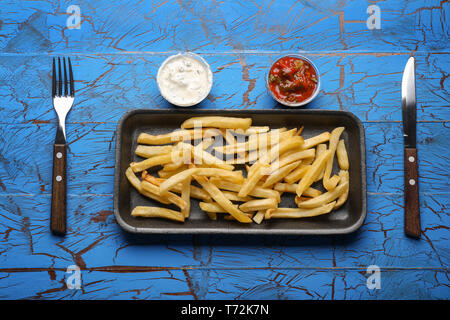 Contenitore con deliziose patatine fritte sul colore di sfondo di legno. Il cibo del servizio di consegna Foto Stock