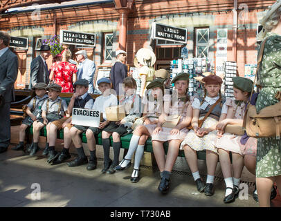 Severn Valley Railway, 1940 eventi bellici, Kidderminster vintage stazione ferroviaria. Ragazzi e ragazze (sfollati) in 1940 abito seduta sul banco in attesa. Foto Stock