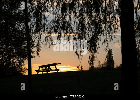 Bella UK tramonto fotografia paesaggio con vista isolata Tavolo picnic in silhouette sulla collina del Regno Unito come molla di sera tramonto nel cielo. Foto Stock