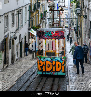 Street car con graffiti in discesa su una strada in pendenza con pedoni e gli edifici residenziali; Lisbona, regione Lisboa, Portogallo Foto Stock